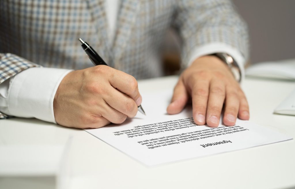 Mężczyzna podpisujący dokument umowy przy biurku