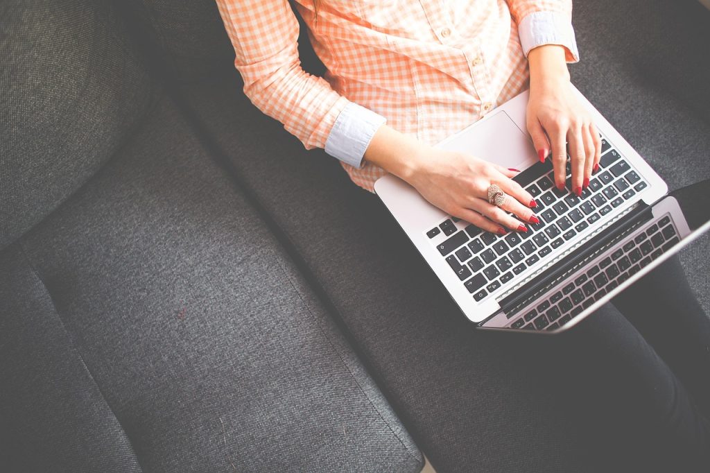 Osoba pisząca na laptopie siedząc wygodnie na kanapie