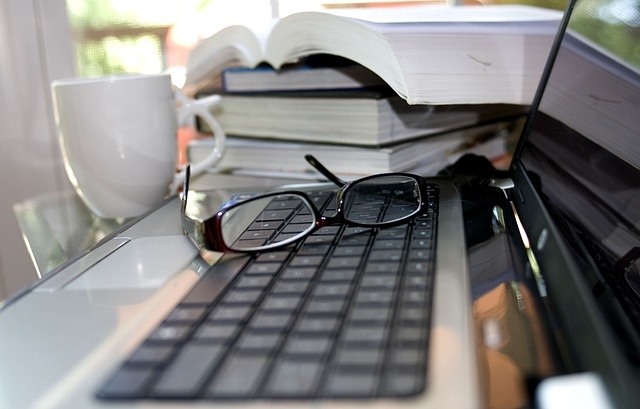 Kompuetr na którym leżą okulary a obok jest stos książek
